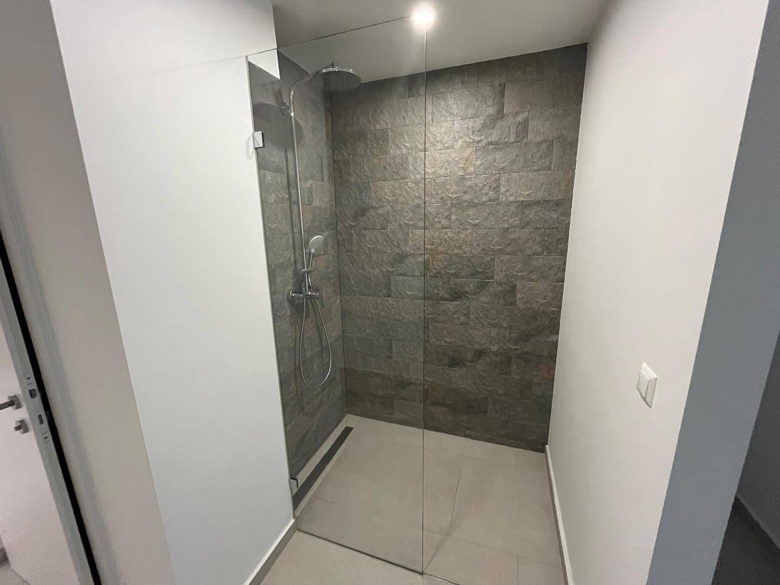 Moderne begehbare Dusche mit dunklen Steinwandfliesen und Glasabtrennung.