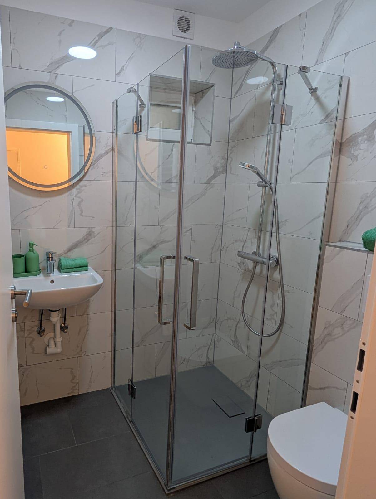 Modernes Badezimmer mit begehbarer Dusche, Marmorfliesen und runden Spiegel.