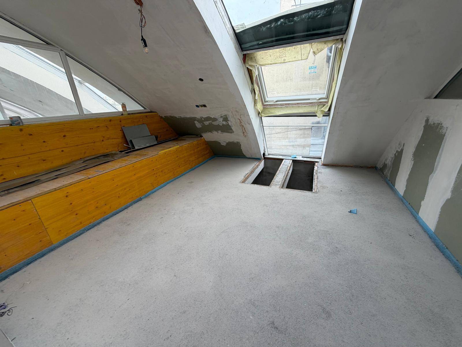 Dachgeschossraum im Bau mit Dachfenster und Holzverkleidung an einer Wand.