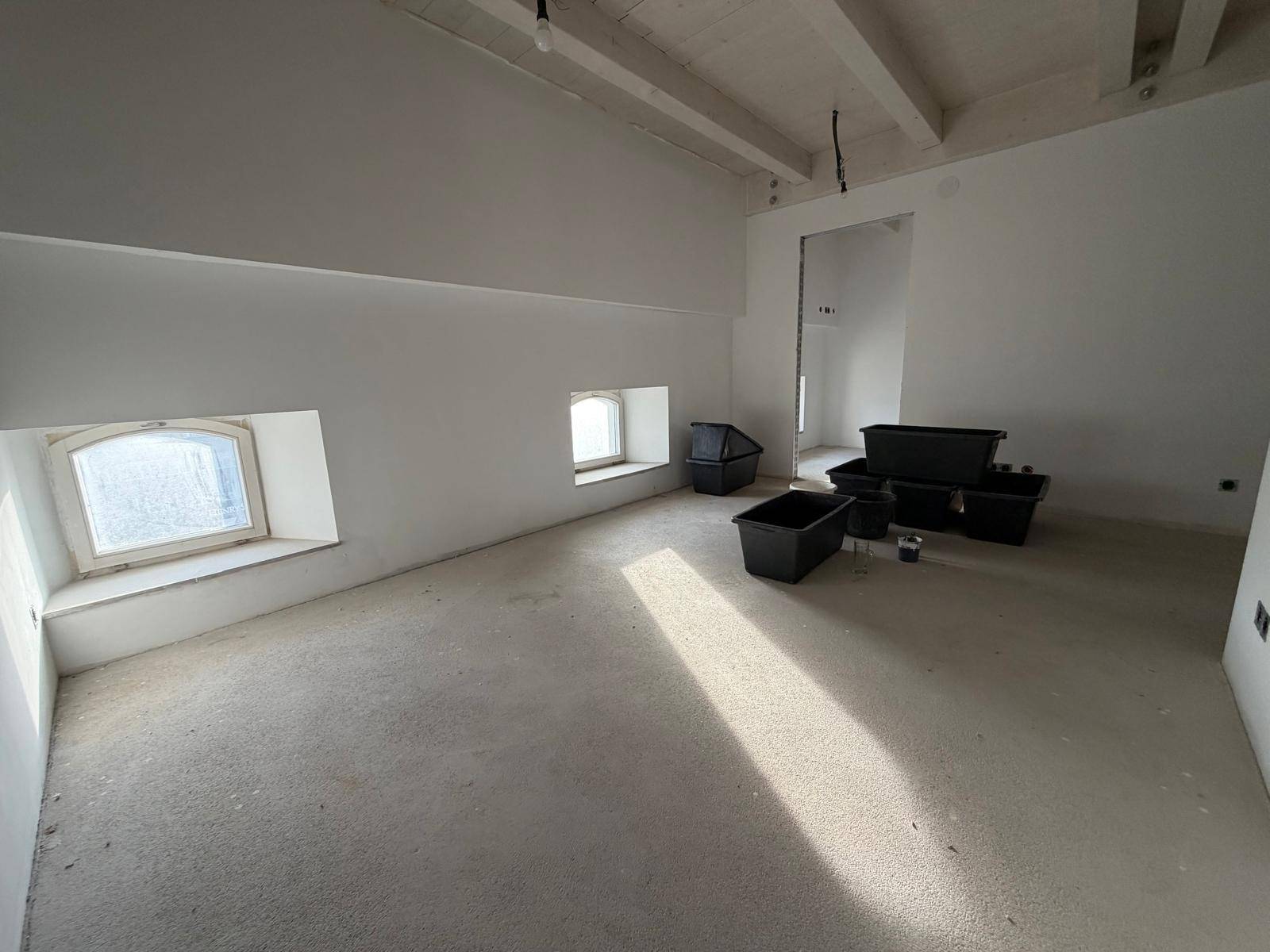 Leerer Raum im Bau mit kleinen Fenstern und viel Tageslicht auf dem Boden.
