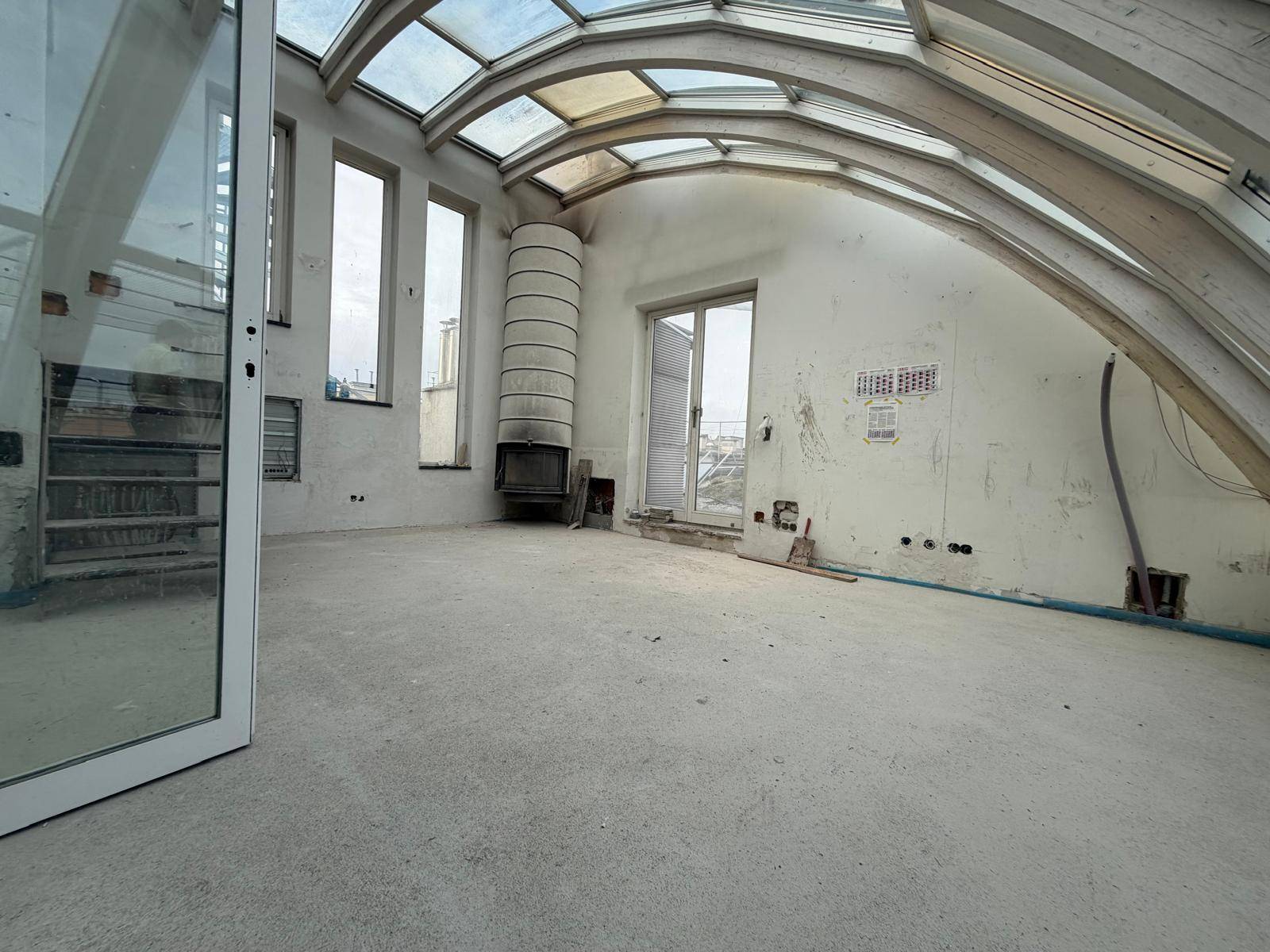 Großer offener Wohnbereich im Bau mit gebogenem Glasdach, Kamin und Zugang zur Terrasse.