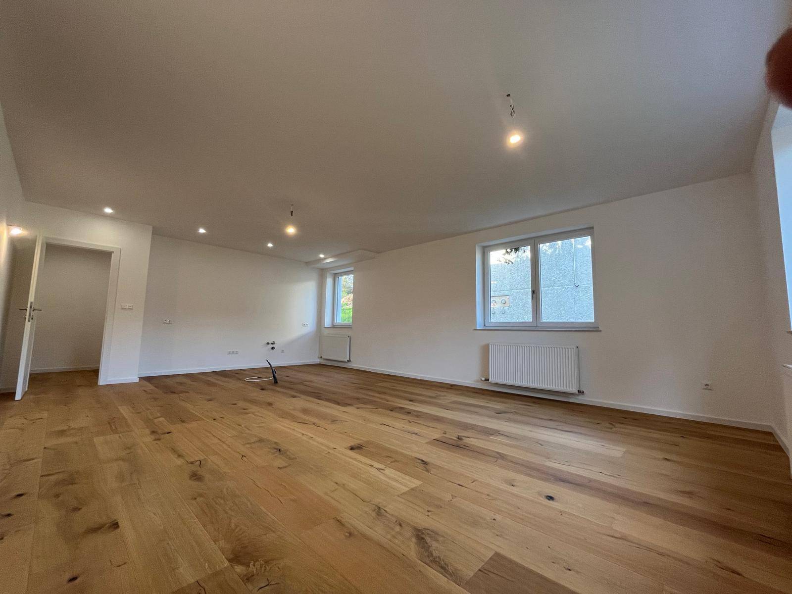 Helles Wohnzimmer mit breiten Holzplanken und mehreren Fenstern für viel Tageslicht.