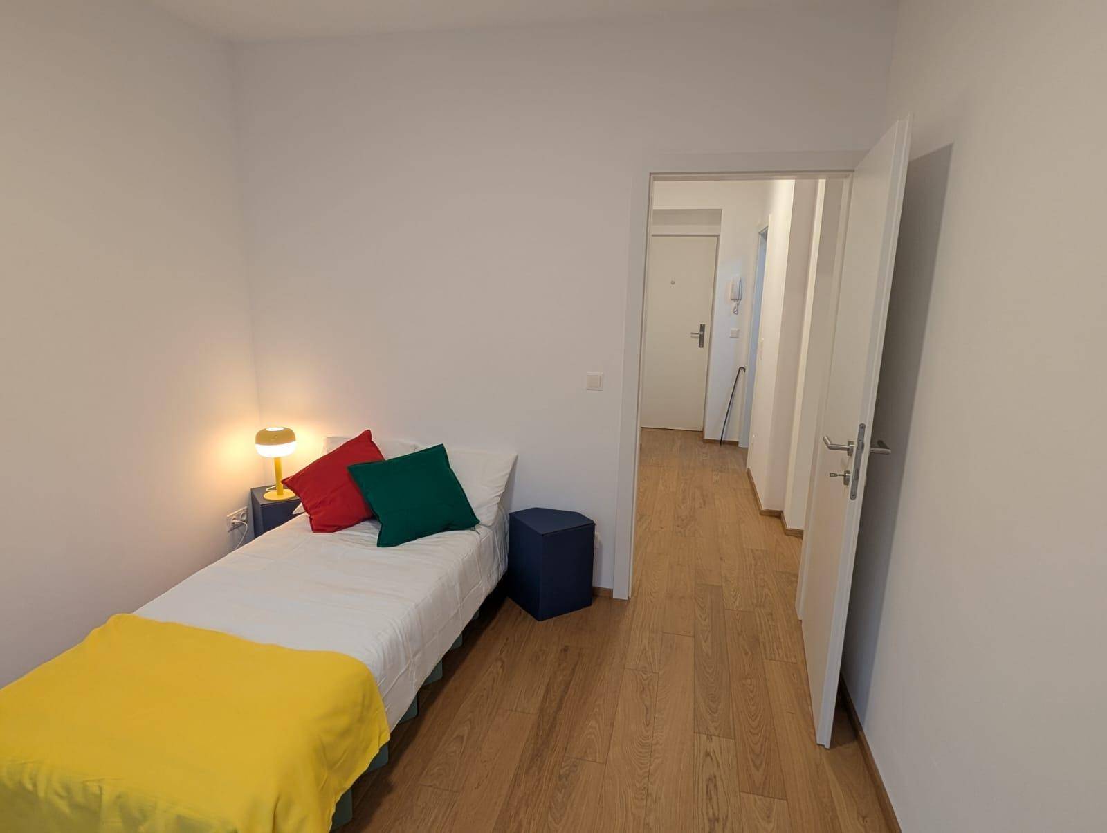 Gemütliches Schlafzimmer mit Holzboden, Einzelbett und farbigen Kissen.
