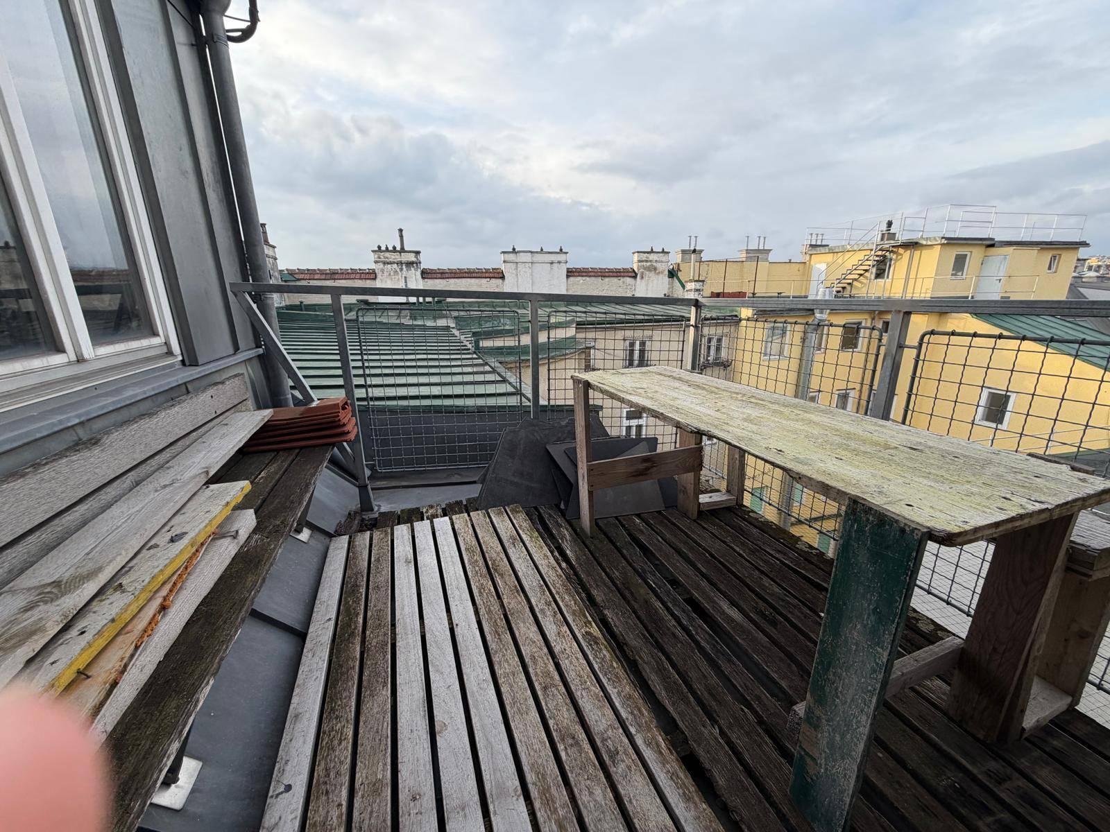 Rustikale Dachterrasse mit Holzboden und Sitzgelegenheiten, umgeben von Dächern.