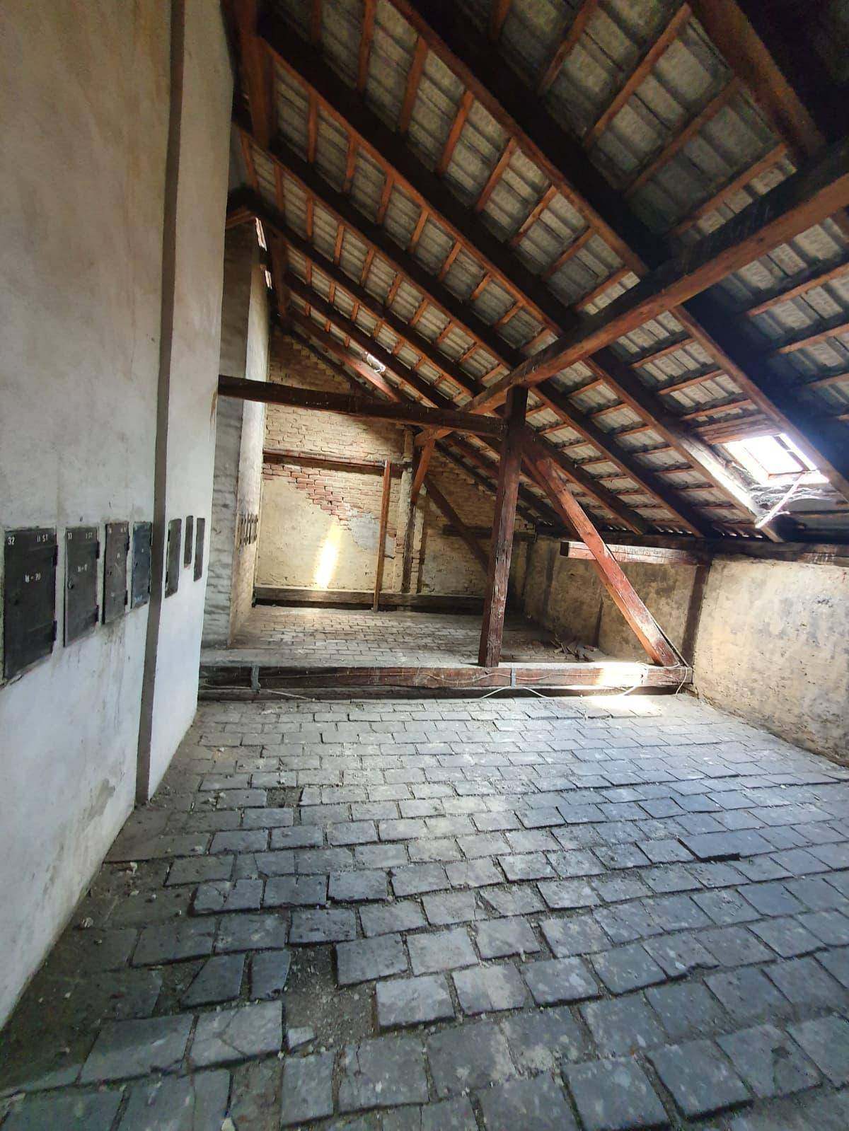 Heller Dachboden mit sichtbaren Holzbalken, Ziegelboden und einem Dachfenster, ideal für Ausbauprojekte.