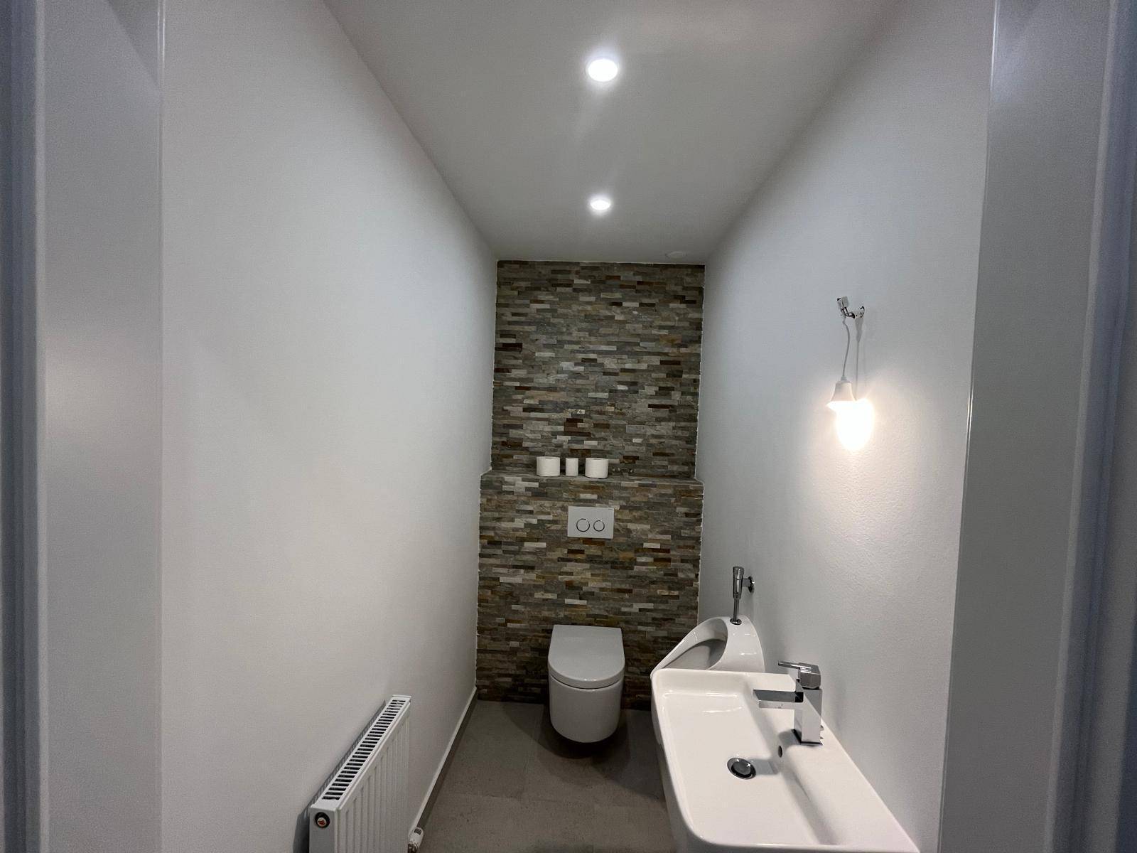 Modernes Gäste-WC mit Wand-WC, Waschbecken und dekorativer Steinwand.