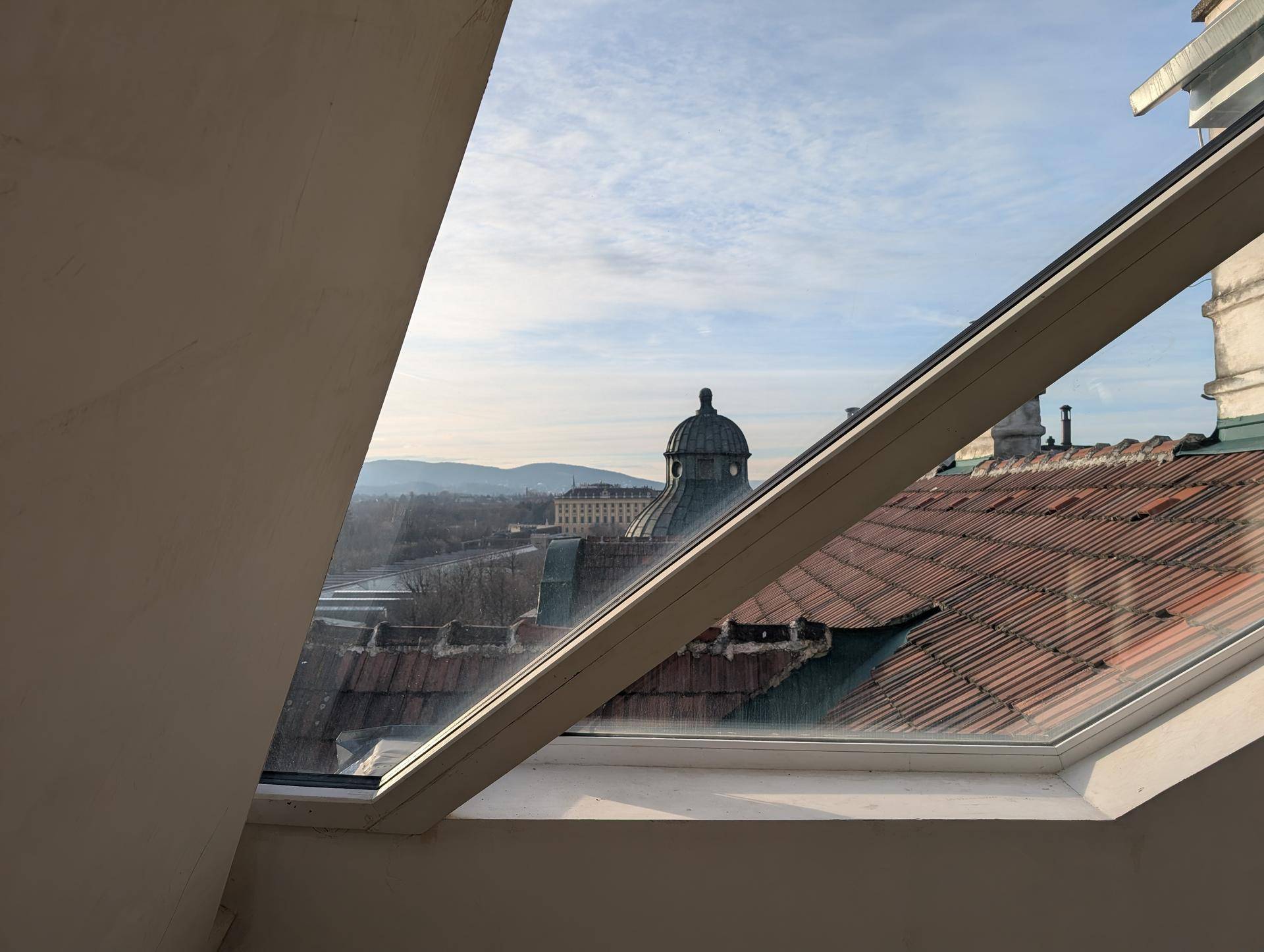 Blick aus einem Dachfenster auf die umliegenden Dächer und eine historische Kuppel.