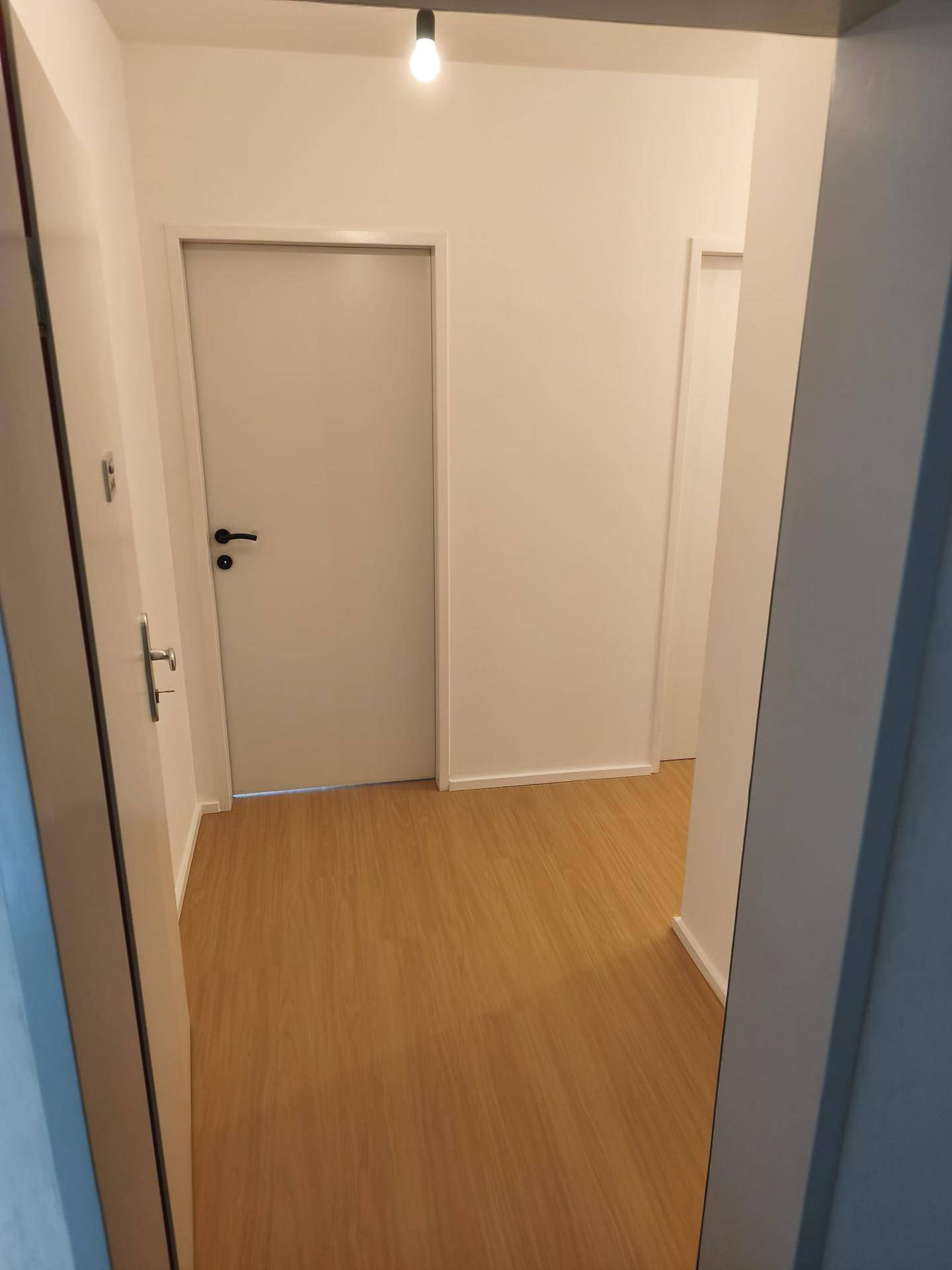 Heller Flur mit Laminatboden und weißen Wänden, der zu den weiteren Räumen führt.