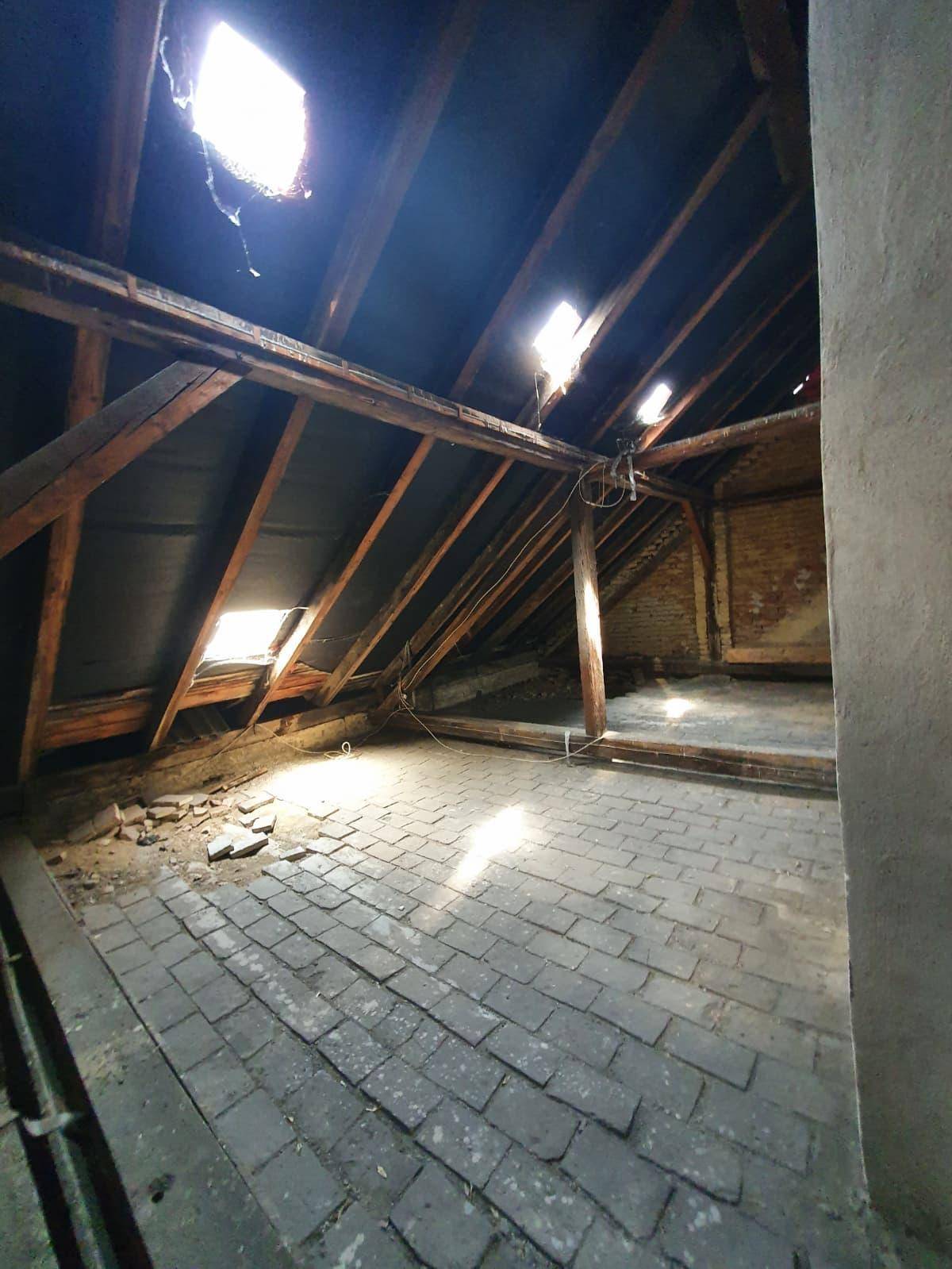Heller Dachboden mit freiliegendem Dachstuhl, Ziegelboden und mehreren Dachfenstern, viel Licht.
