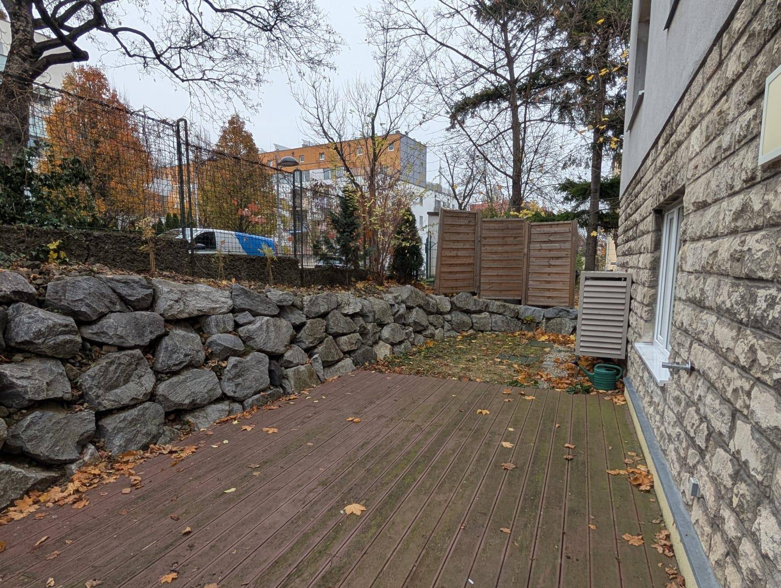 Blick auf die Holzterrasse mit Steinmauer und angrenzendem Gartenbereich im Herbst.