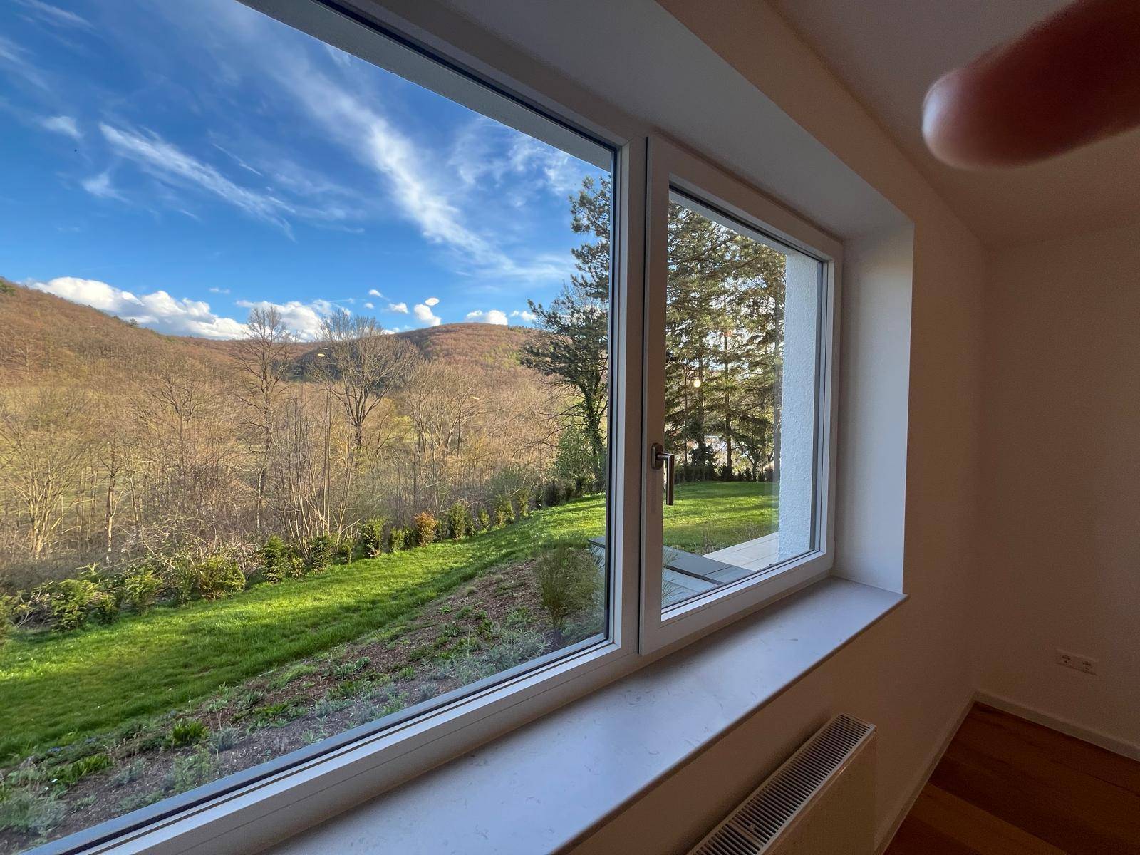 Innenraum mit Fenster und Ausblick auf die grüne Umgebung und bewaldete Hügel.