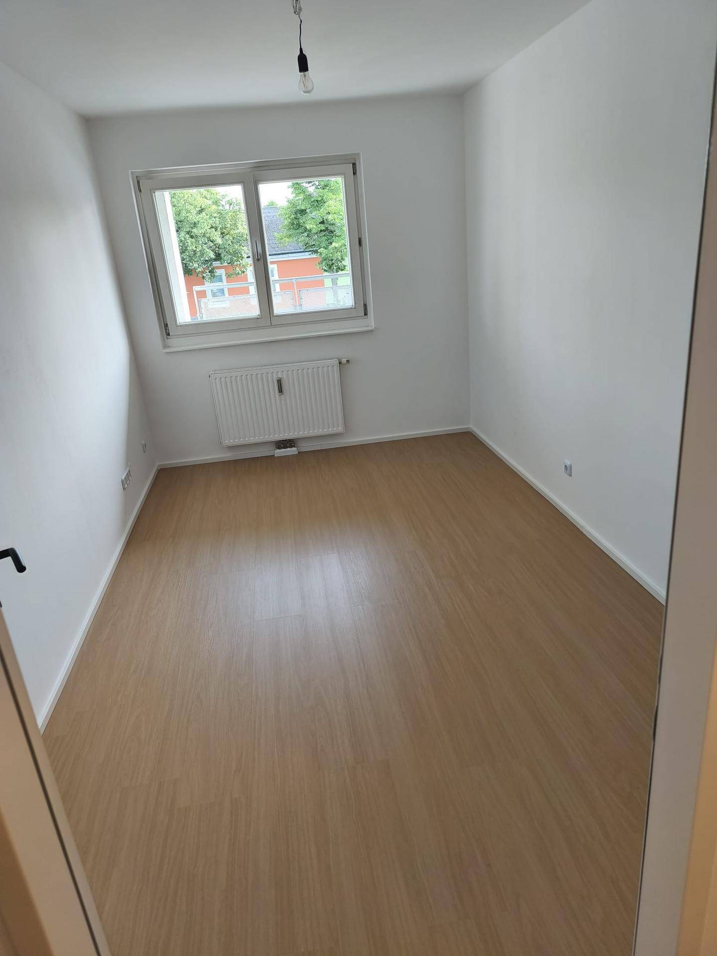 Geräumiges Schlafzimmer mit hellem Laminatboden und großem Fenster für viel Tageslicht.