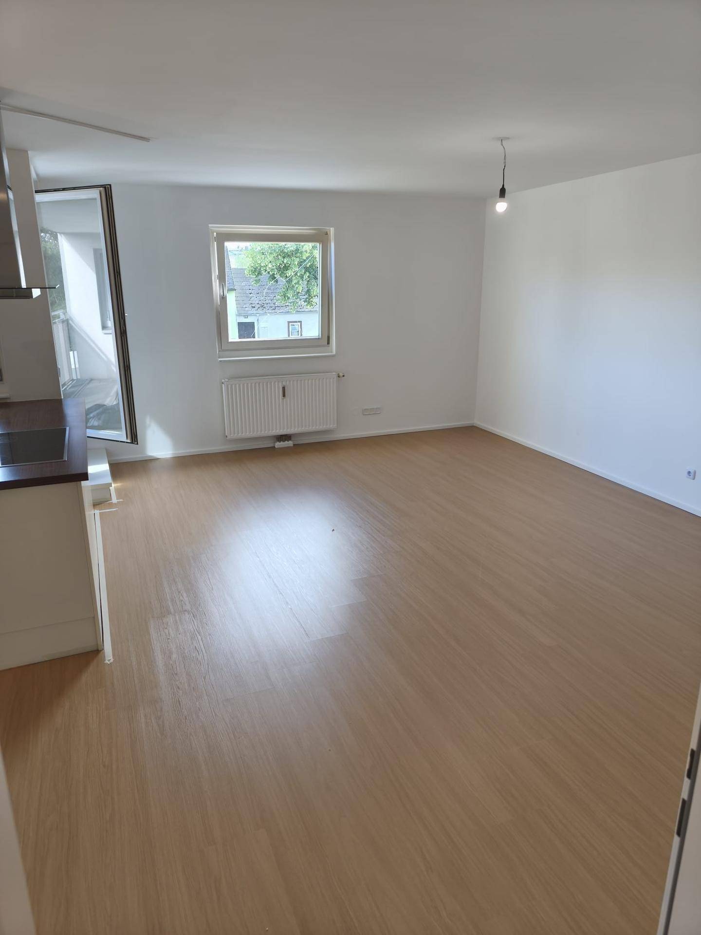 Heller Wohnbereich mit Laminatboden, großem Fenster und Heizkörper.