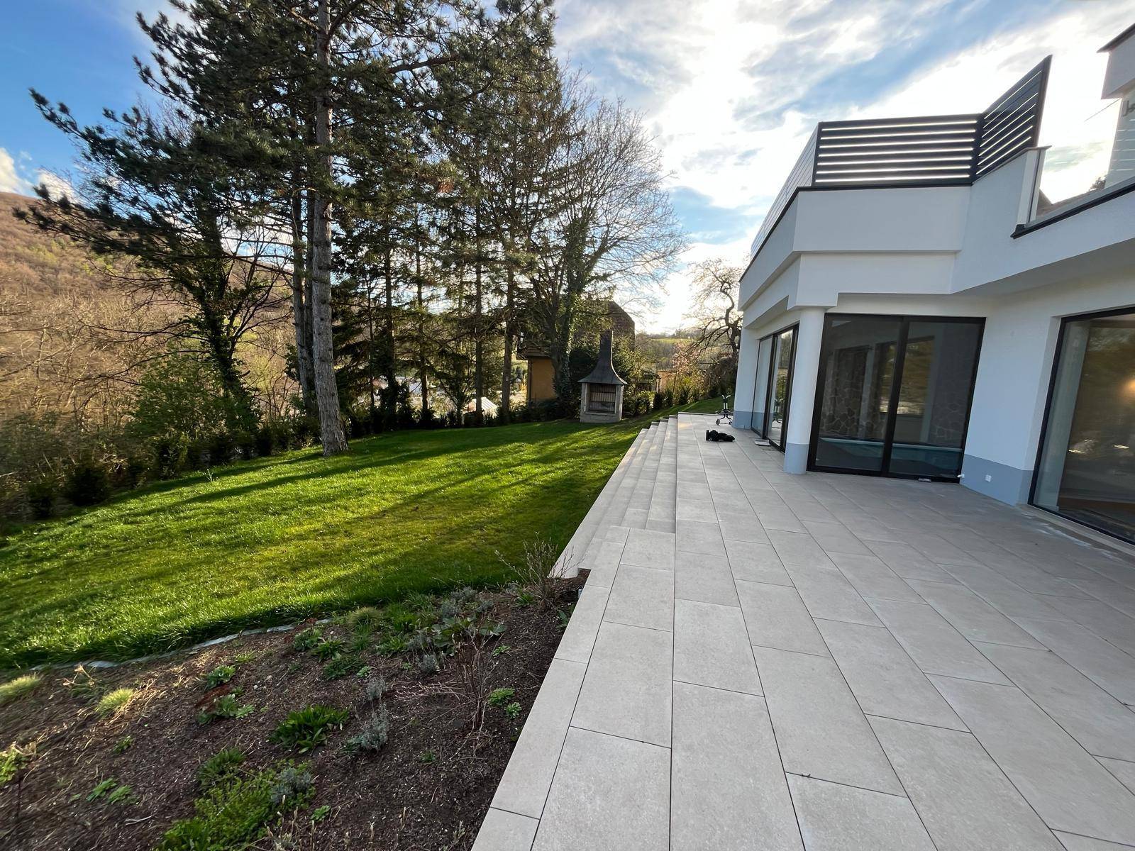 Geräumige Terrasse mit Fliesenboden und angrenzendem Rasenbereich, ideal für Entspannung im Freien.