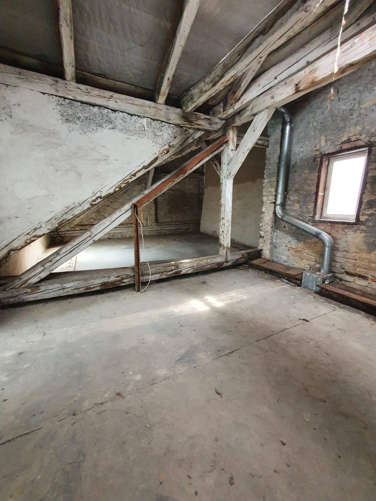 Geräumiger Dachboden mit freiliegenden Holzbalken und einem kleinen Fenster in der Ziegelwand.