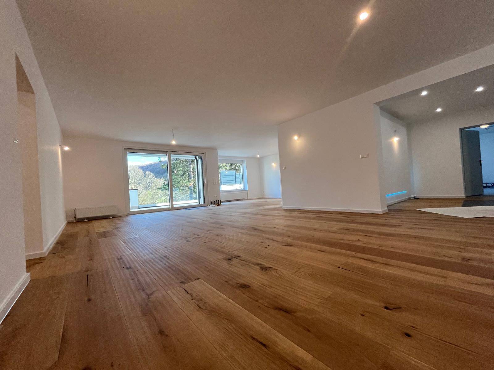 Geräumiger Wohnbereich mit hellem Holzparkett und großen Schiebetüren zur Terrasse.