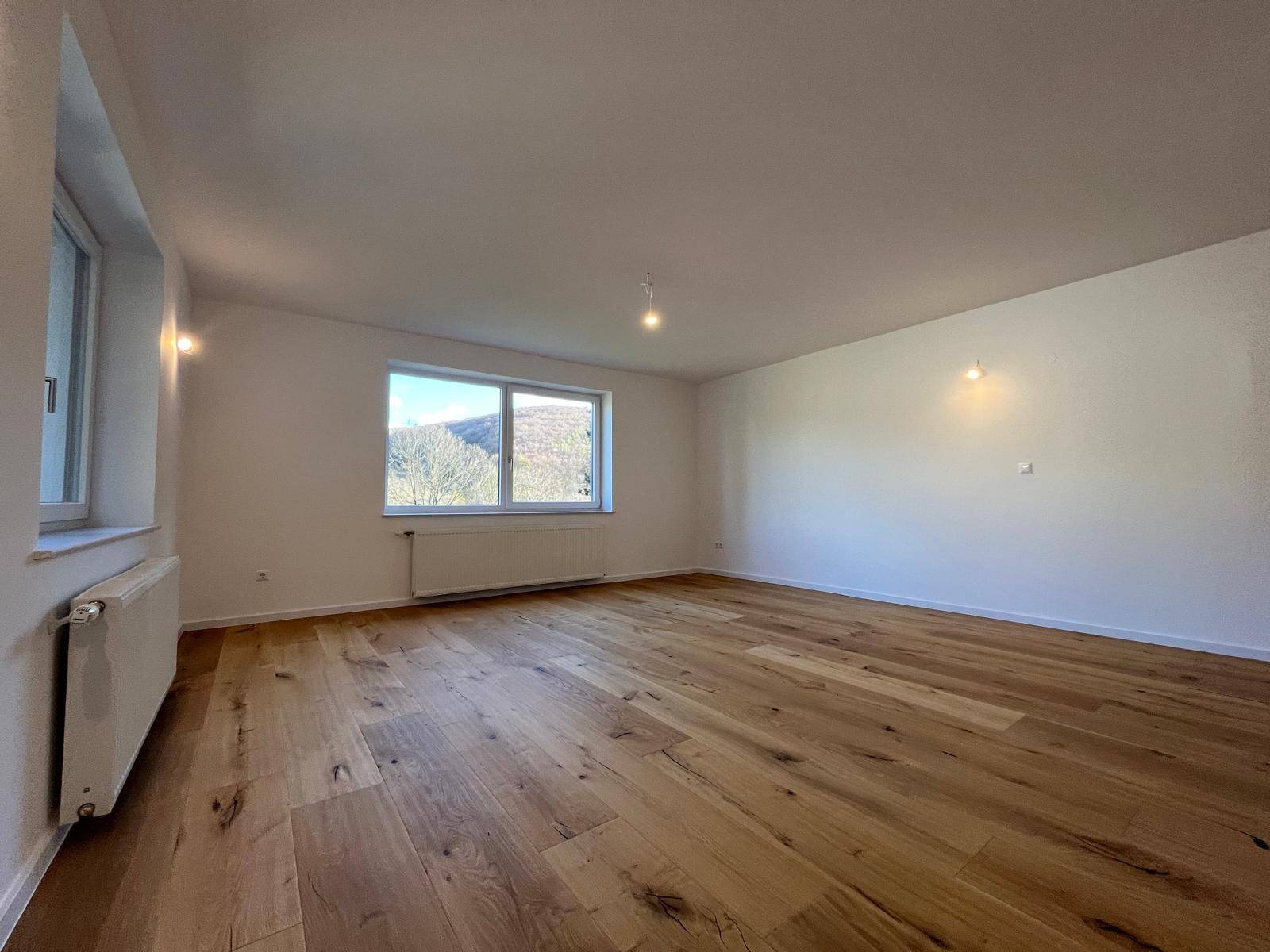 Geräumiges Zimmer mit Holzparkett und Fenster mit Blick auf die Natur.