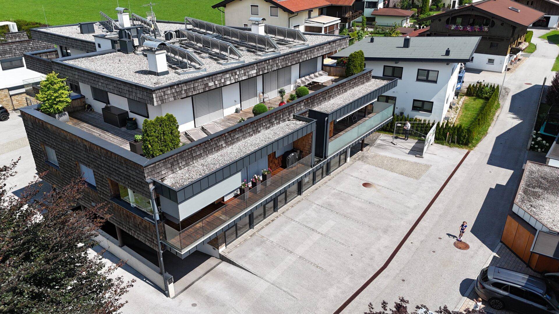 Modernes Mehrfamilienhaus mit Flachdach, Photovoltaikanlage und mehreren Balkonen in ländlicher Umgebung.