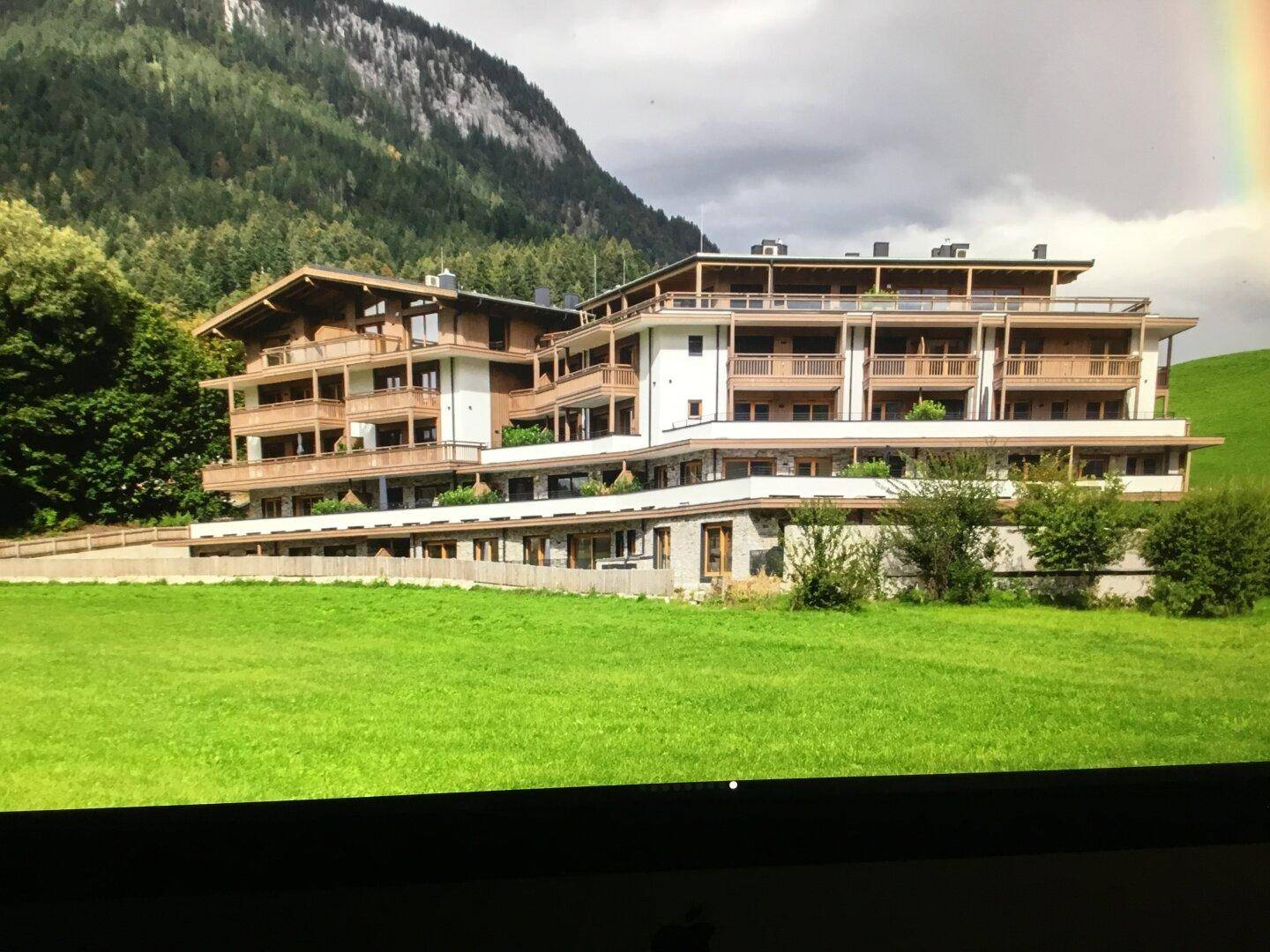 Großes Wohngebäude in alpiner Landschaft mit vielen Balkonen und grüner Umgebung, modern gestaltet.