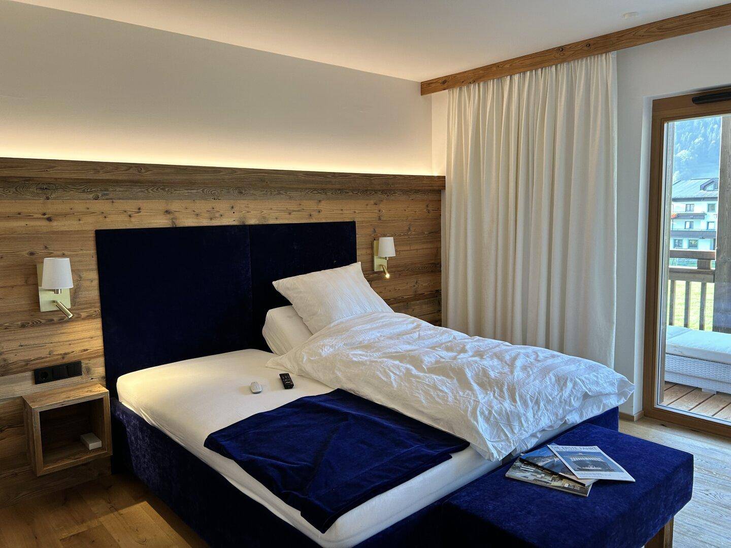 Helles Schlafzimmer mit bequemem Bett, Holzboden und Zugang zu einem sonnigen Balkon mit Bergblick.