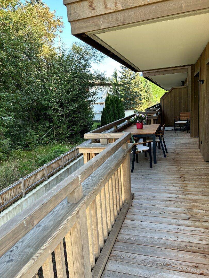 Geräumiger Holzbalkon mit Esstisch und Stühlen, umgeben von grüner Landschaft und Bergblick.