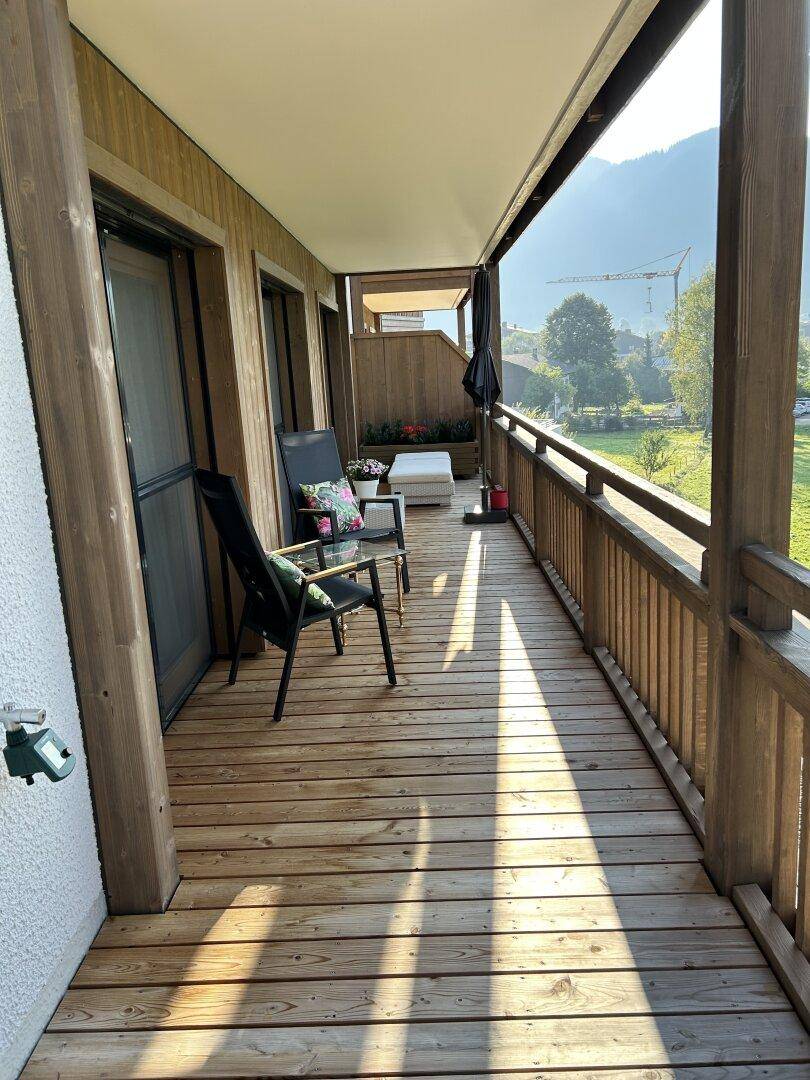 Sonniger Holzbalkon mit Sitzmöglichkeiten und weitem Blick auf die Berge und grüne Umgebung.