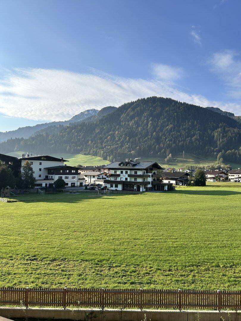 Weitläufige Landschaft mit grünen Wiesen, Bergen und umliegenden Gebäuden an einem sonnigen Tag.
