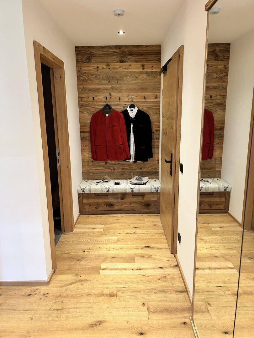 Heller Flur mit Holzboden, Garderobe und großem Spiegel, einladend und funktional gestaltet.