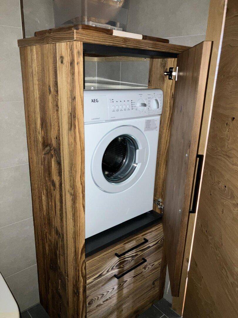 Praktischer Waschmaschinenbereich in einem Holzschrank integriert, platzsparend und funktional im Badezimmer.