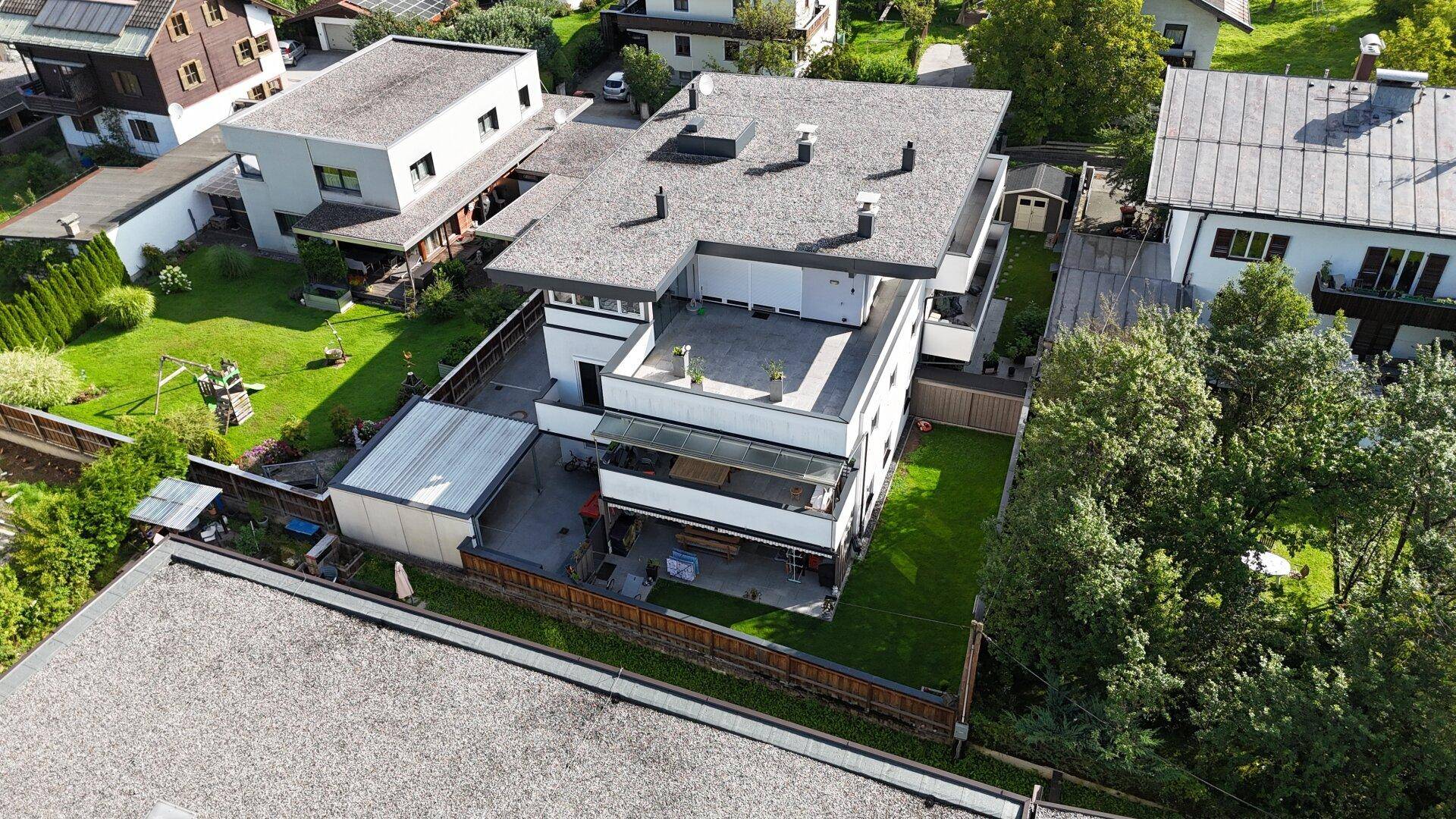 Luftaufnahme eines modernen Gebäudes mit Flachdach, mehreren Terrassen und umliegenden Grünflächen.