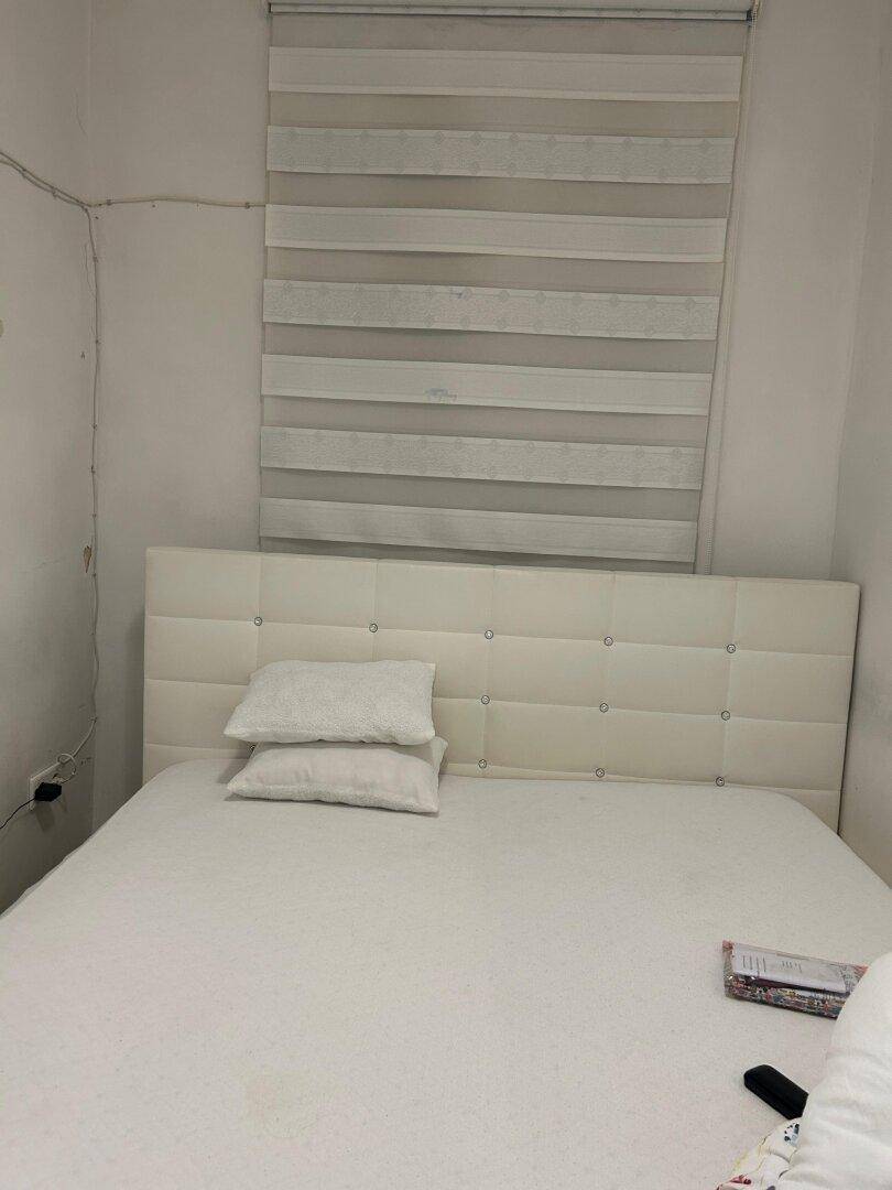 Schlafzimmer mit weißem Polsterkopfteil und einem Bett, Fenster mit Jalousien für Privatsphäre.