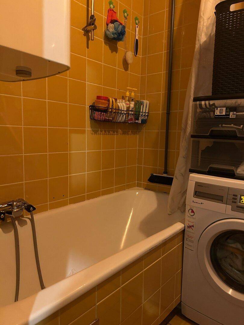 Badezimmer mit gelben Fliesen, einer Badewanne und einer Waschmaschine, funktional eingerichtet.