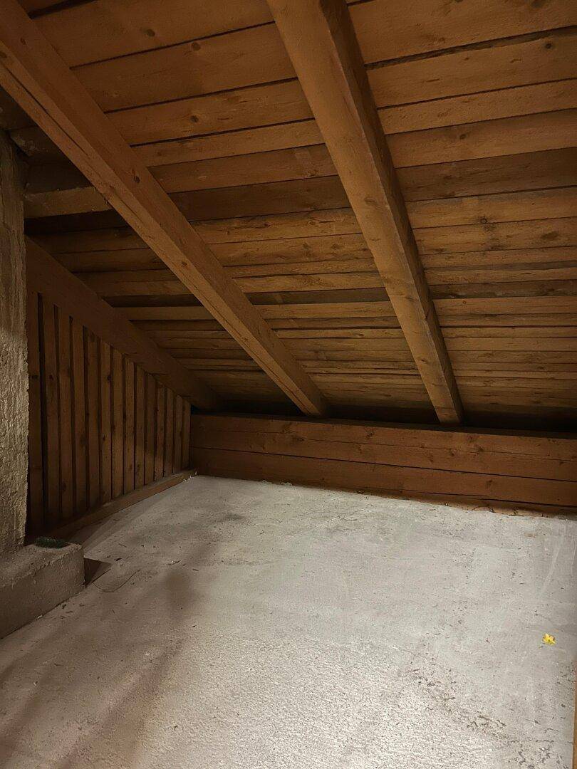 Dachboden mit sichtbaren Holzbalken und Betonboden, bietet ungenutzten Stauraum.