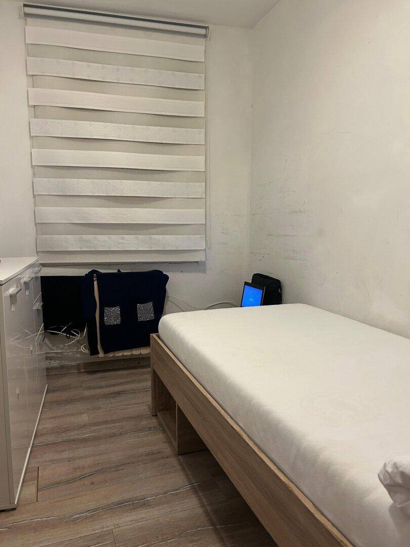 Schlafzimmer mit Einzelbett und Kommode, ausgestattet mit Laminatboden und Fenster mit Jalousien.