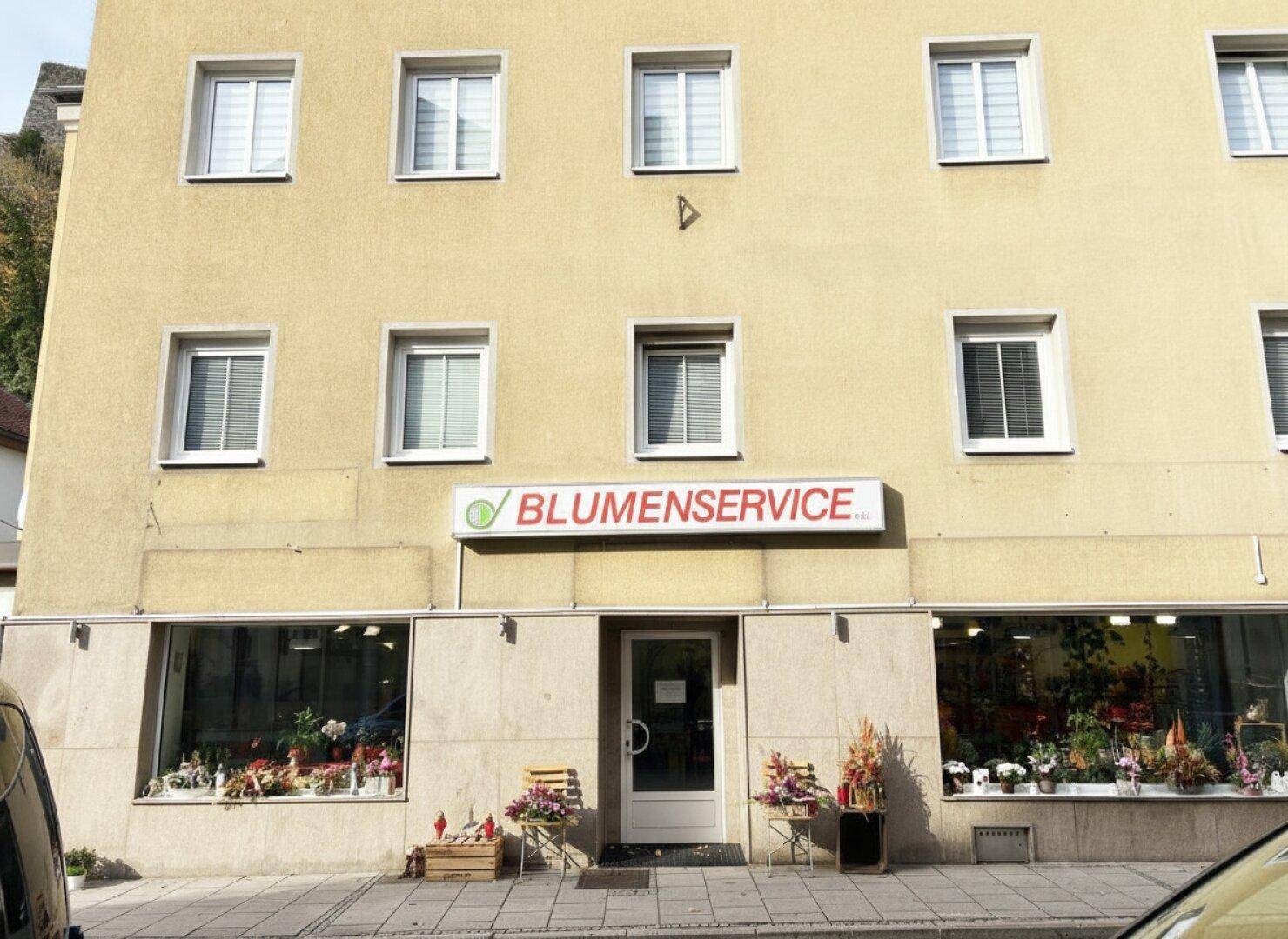 Nahaufnahme der Ladenfront im Erdgeschoss mit Eingangstür und großen Schaufenstern des Blumenladens.