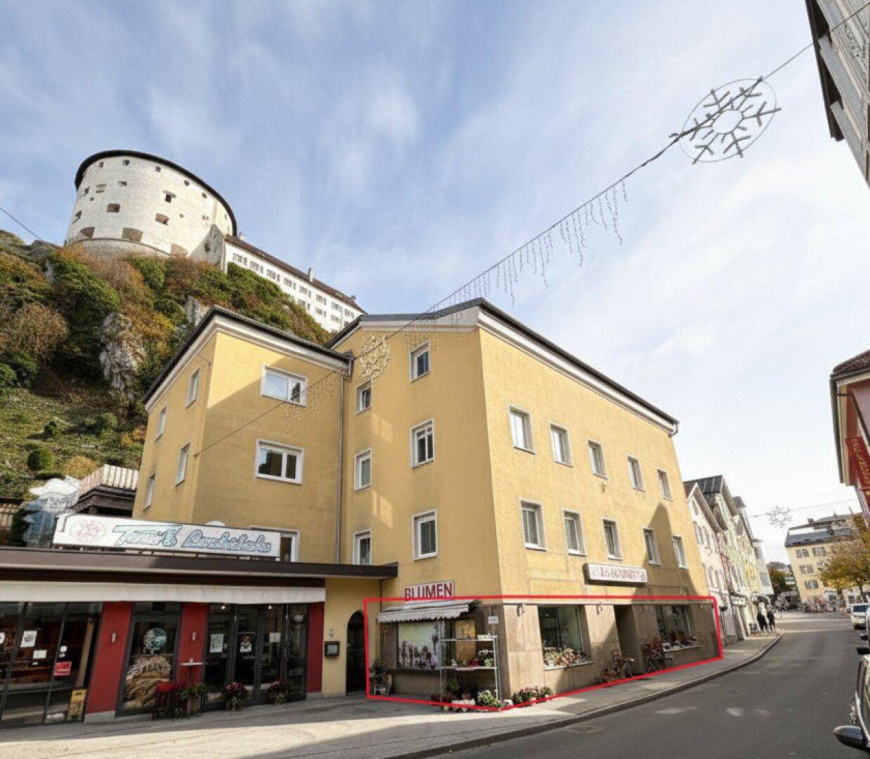 Außenansicht des Gebäudes mit Geschäftslokal im Erdgeschoss und Blick auf die umliegende Stadtlandschaft und Burg.