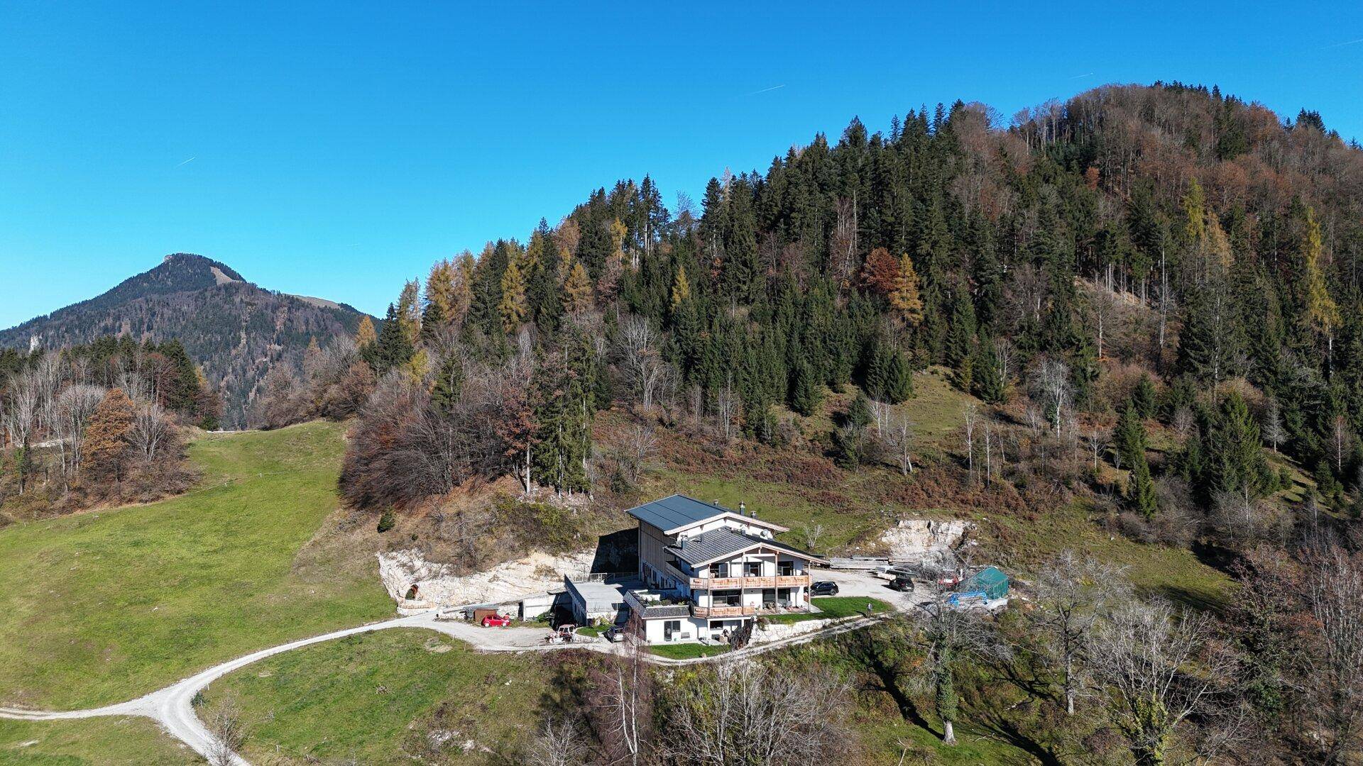 Luftaufnahme eines ländlichen Anwesens mit Wald und Bergen im Hintergrund.