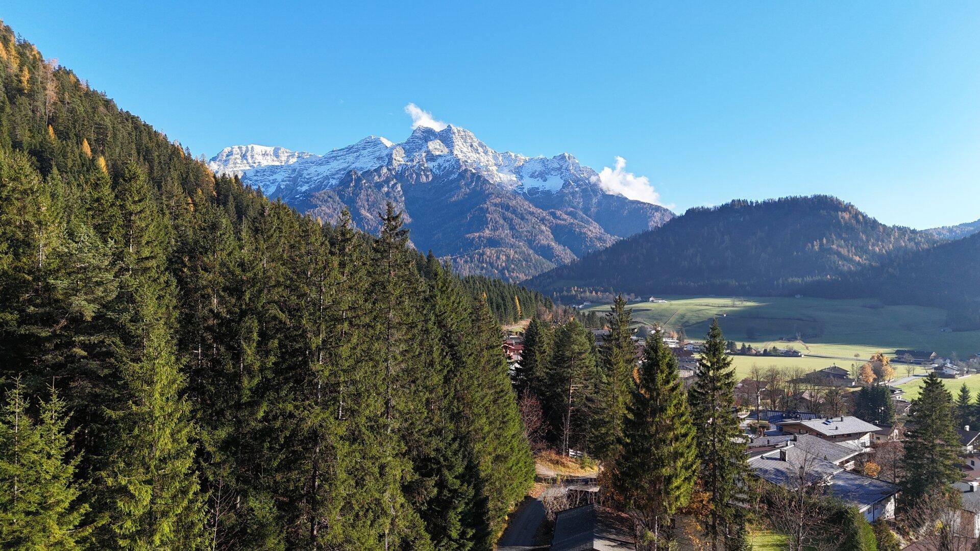 Beeindruckender Bergblick mit schneebedeckten Gipfeln, umgeben von dichten Nadelwäldern unter blauem Himmel.