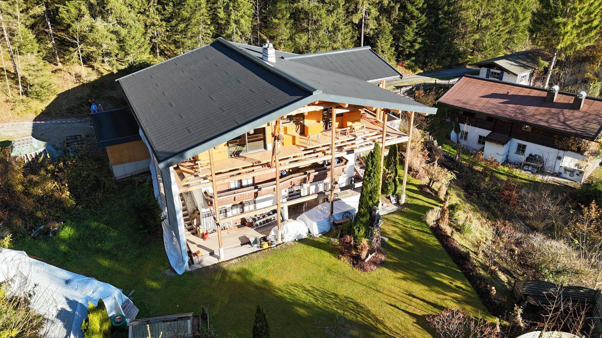 Luftaufnahme eines im Bau befindlichen Chalets, umgeben von dichtem Wald und alpiner Landschaft.