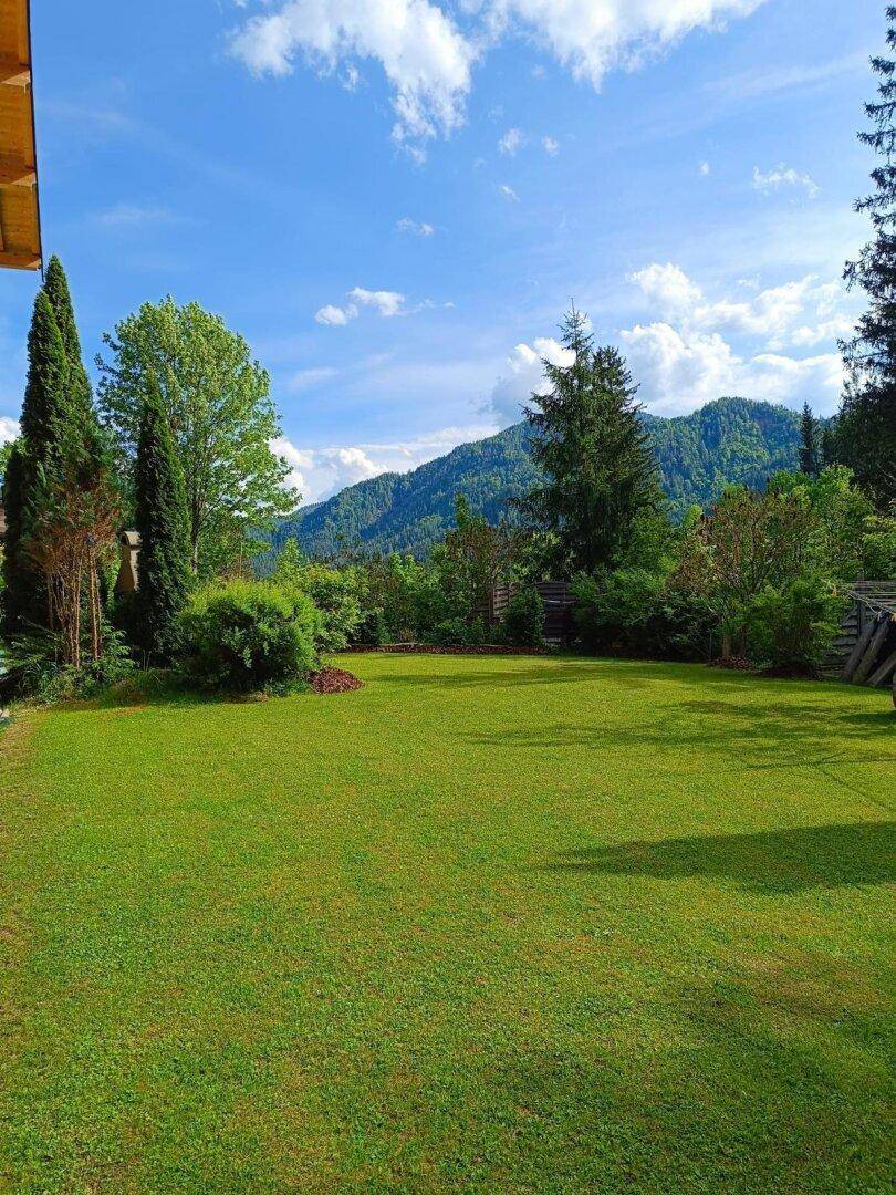 Weitläufige Rasenfläche im Garten mit Blick auf die umliegenden bewaldeten Berge unter blauem Himmel.