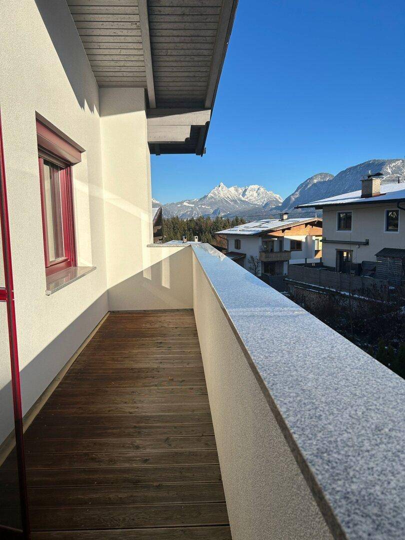 Sonniger Balkon mit Holzboden und beeindruckendem Bergblick unter blauem Himmel.
