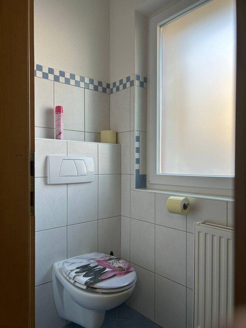 Helles Gäste-WC mit Fenster, Wand-WC und dekorativen Fliesen in Weiß und Blau.