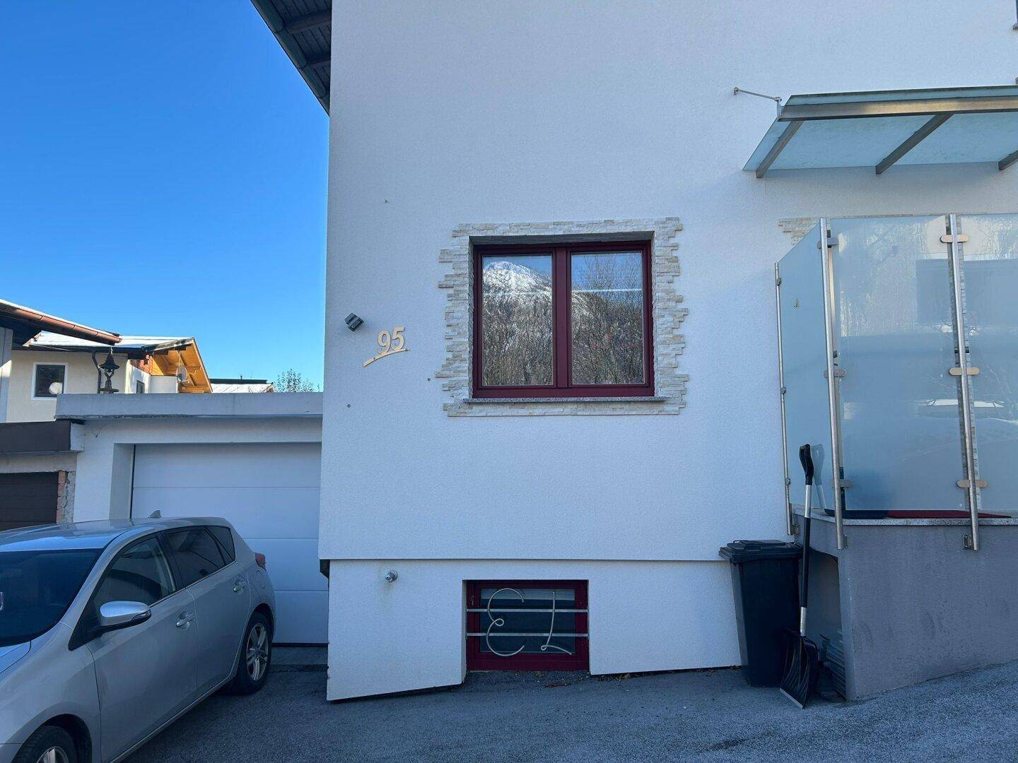 Fassade des Hauses mit Fenster, Einfahrt und geparktem Auto vor der Garage.