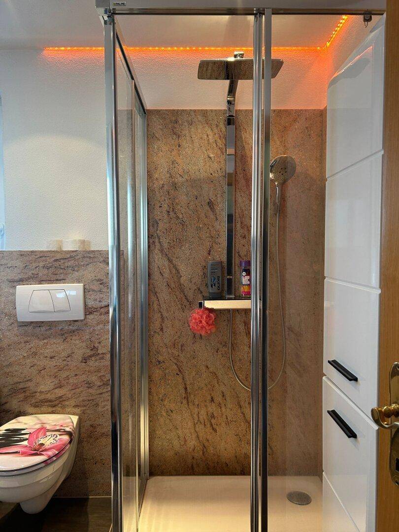 Duschbereich im Badezimmer mit Regendusche, modernen Fliesen und indirekter Beleuchtung an der Decke.