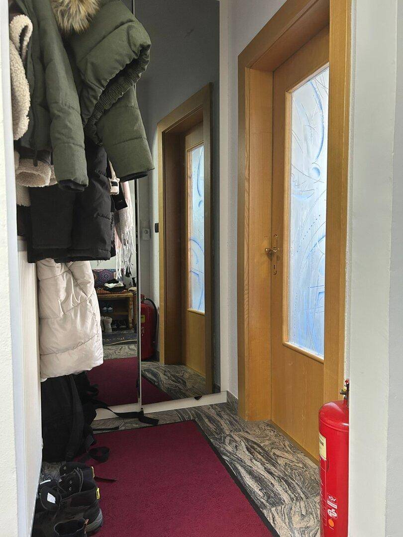 Eingangsbereich mit Garderobe, großem Spiegel und Holztüren, die zu weiteren Räumen führen.