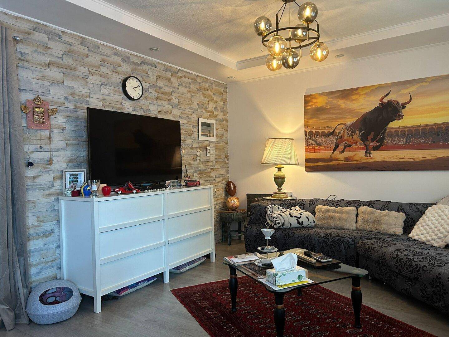 Gemütliches Wohnzimmer mit Steinwand, großem Fernseher und bequemer Sofalandschaft mit dekorativen Kissen.