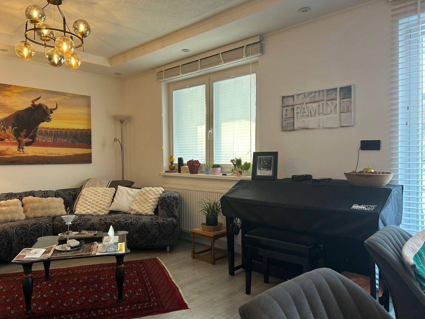 Helles Wohnzimmer mit bequemer Couch, Klavier und großen Fenstern für viel Tageslicht.