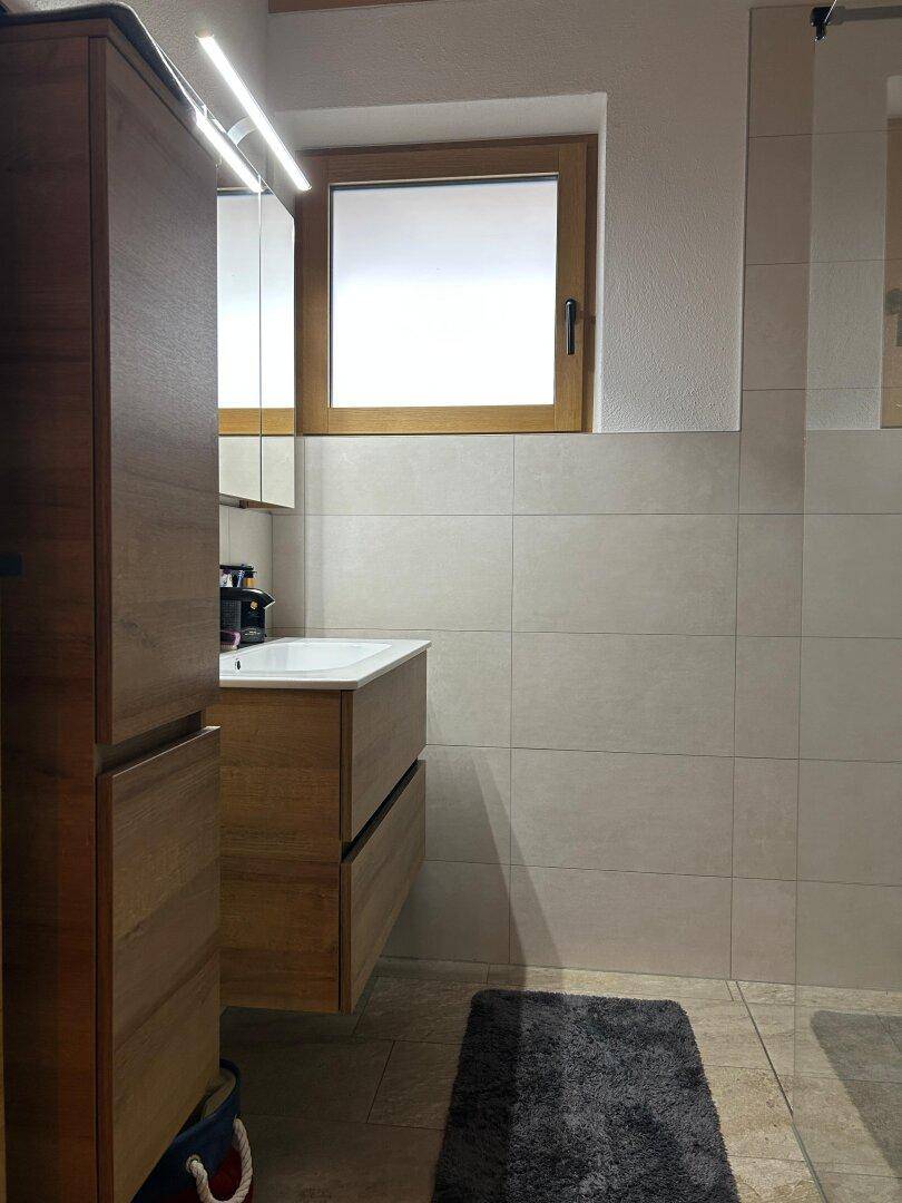 Helles Badezimmer mit Holzwaschtisch, Spiegelschrank und Fenster.