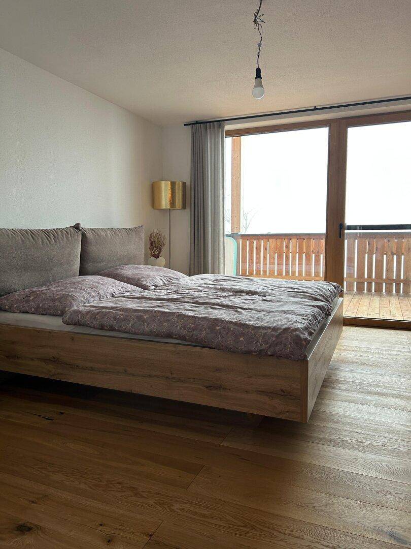 Helles Schlafzimmer mit Holzboden und Zugang zu einem Balkon.