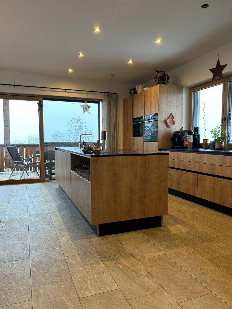 Moderne Küche mit Holzfronten, Kücheninsel und Zugang zu einem Balkon mit Aussicht.